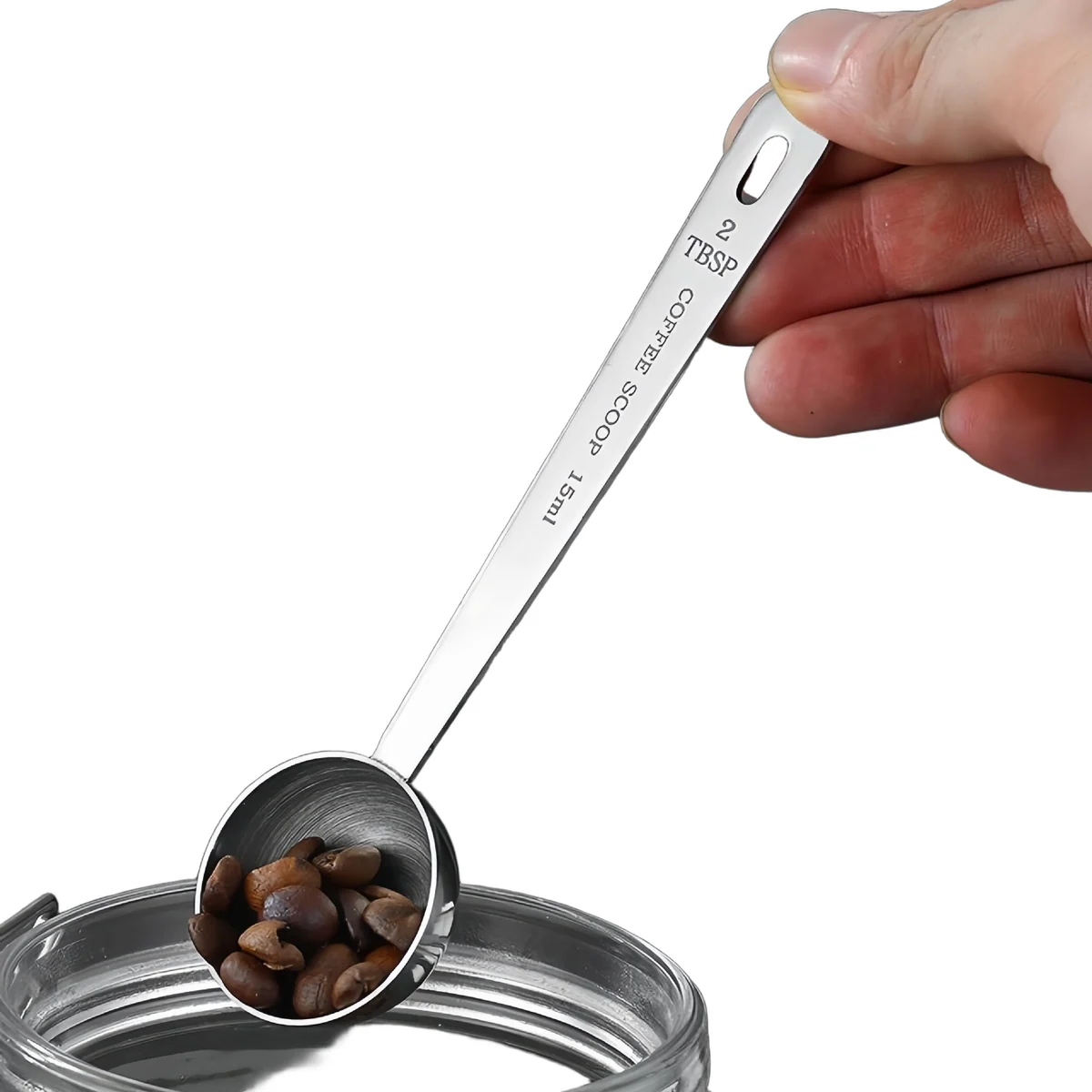 Long-handle stainless scoop lifting coffee beans from a jar