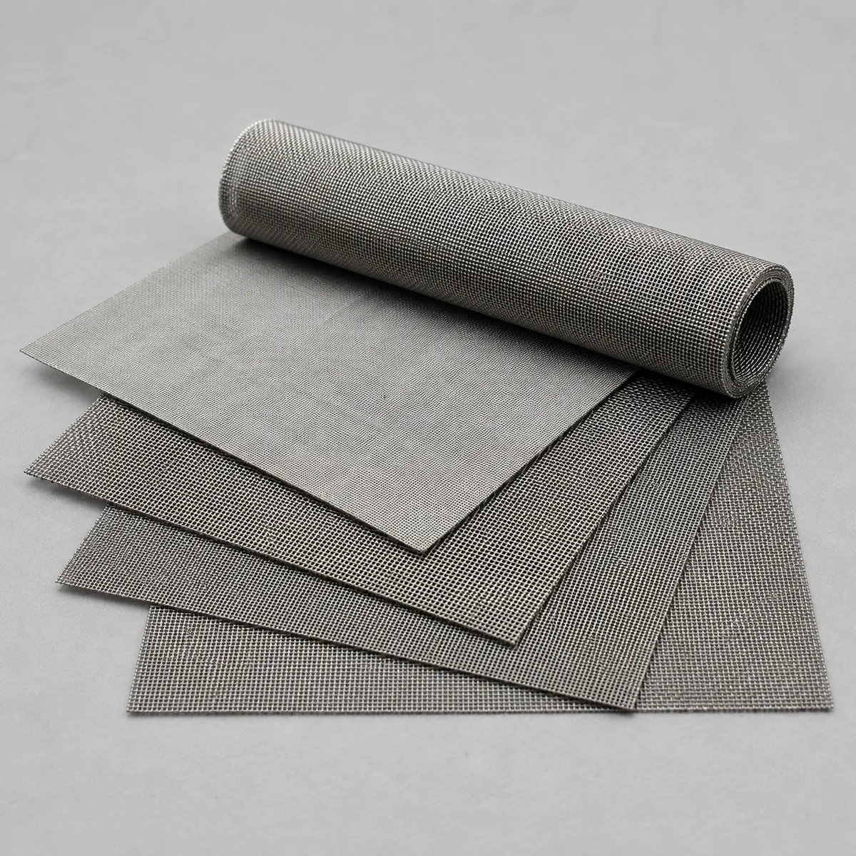 Stainless steel filter mesh sheets and roll on a clean grey background