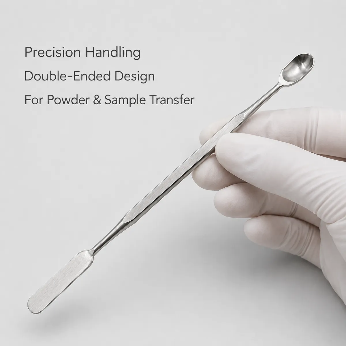 Double-ended stainless steel spatula held by a gloved hand for sample handling