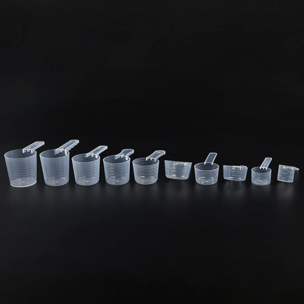 Graduated plastic measuring cups lined up from large to small on a dark background
